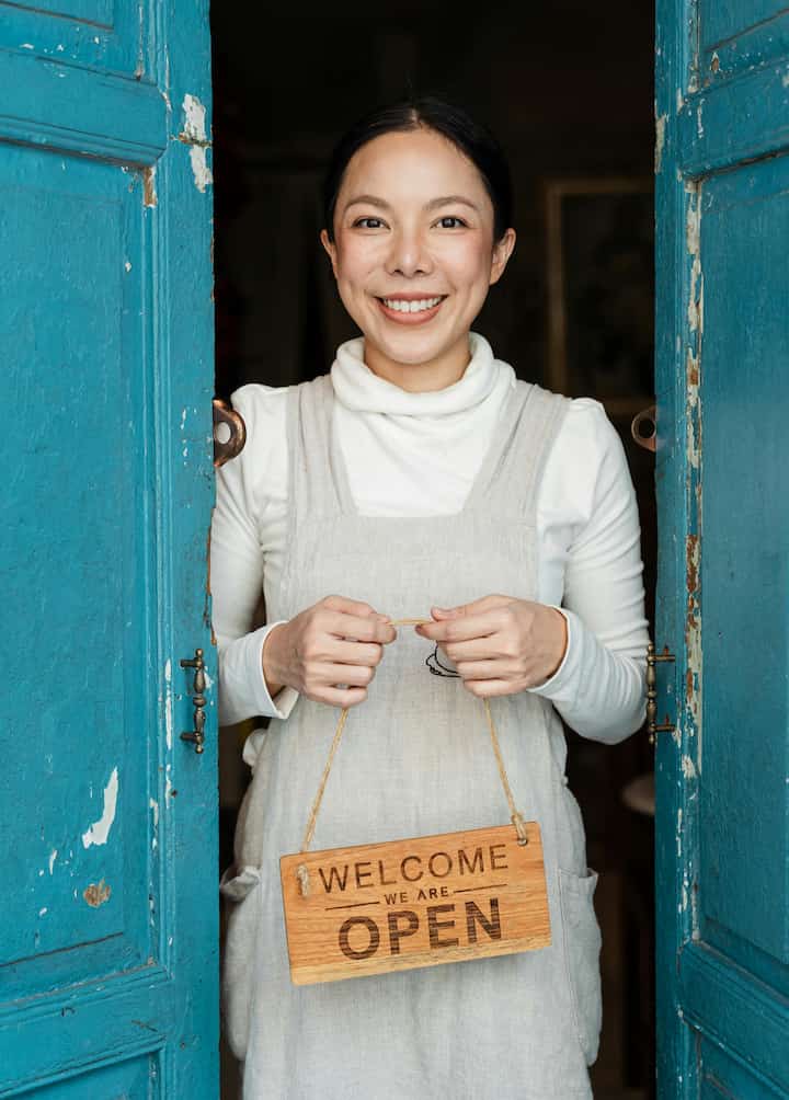 Smiling woman holding a sign that says "we're open"